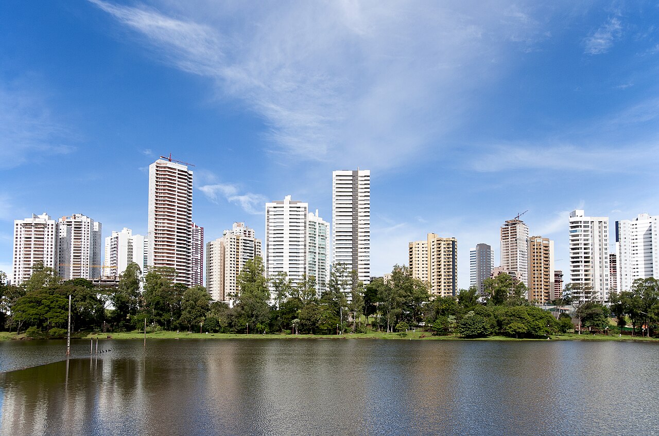 Prédios residenciais às margens do Lago Igapó, em Londrina, Paraná, com árvores na orla e céu azul